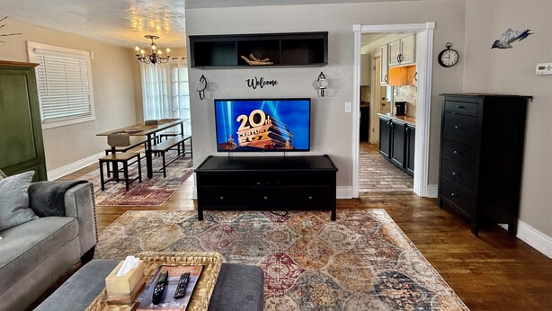 A living room with a flat-screen TV, a sofa, a coffee table, and a dining area with a bench. - Garden Cottage | Close to SLC (Midvale)