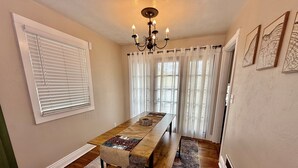 A dining area with a long wooden table, two benches, a chandelier, and a patterned rug. - Garden Cottage | Close to SLC (Midvale)