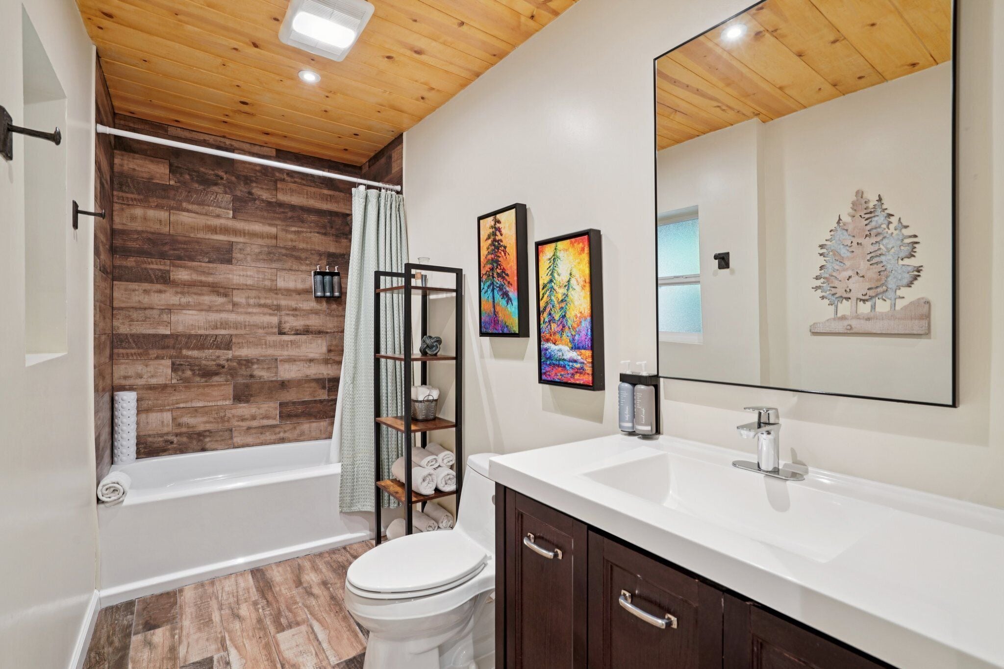 Une salle de bain moderne avec un plafond en bois, une baignoire blanche, des toilettes blanches et un grand miroir au-dessus du lavabo.