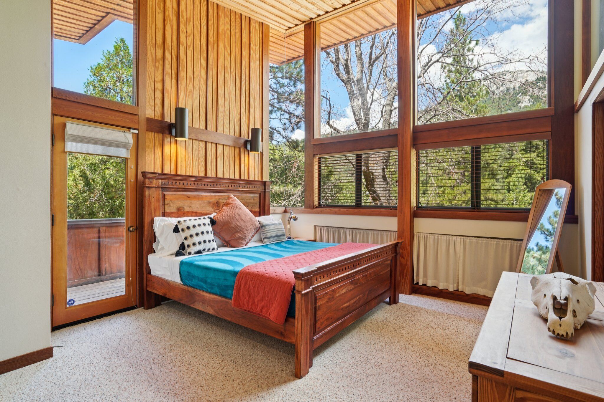 Un dormitorio con una cama de madera, una mesita de noche y un ventanal con vistas a árboles.