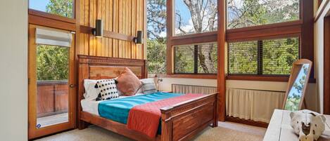 Un dormitorio con una cama de madera, una mesita de noche y un ventanal con vistas a árboles.
