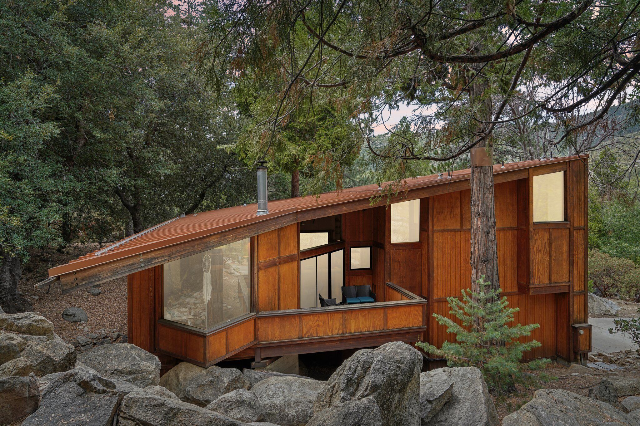 A wooden cabin with large windows, a balcony, and a view of the surrounding forest.