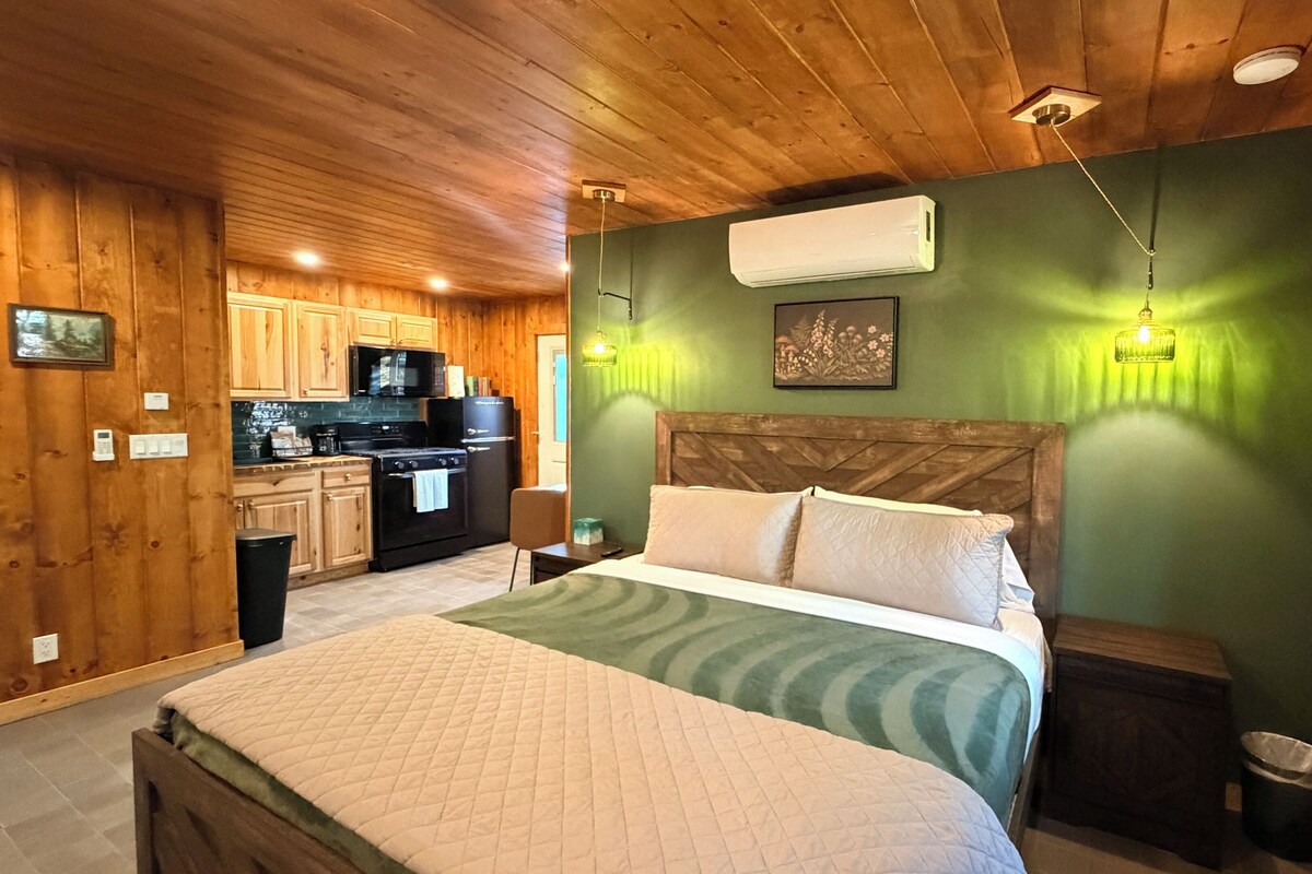 A room with a bed, a wooden ceiling, a kitchen area, and a green wall.