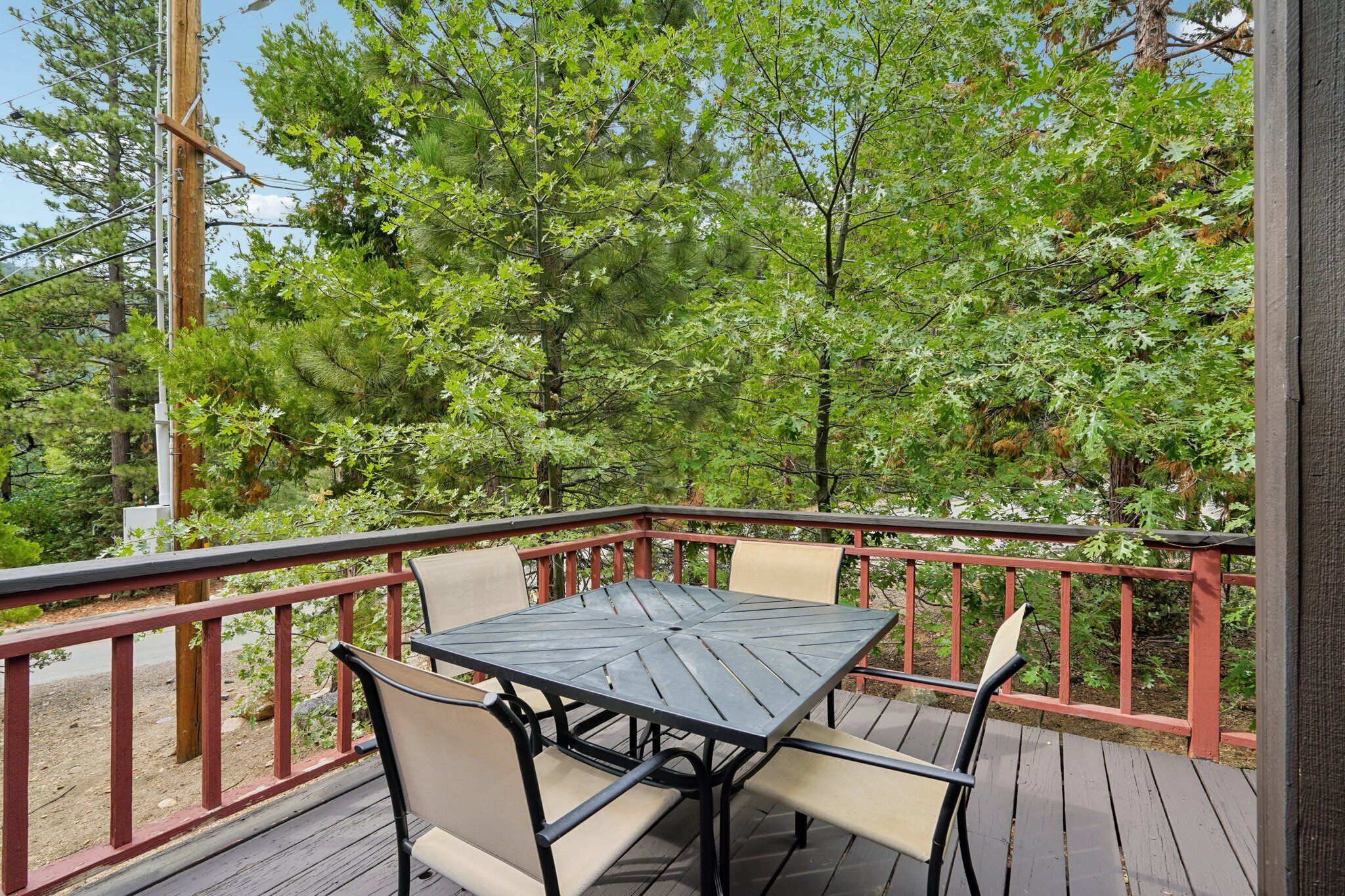 A deck with a square table and four chairs, surrounded by a red railing, overlooking a forested area.