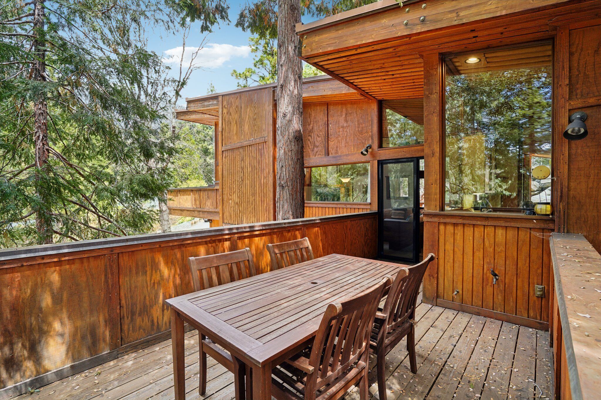 A wooden deck with a table and chairs, surrounded by trees.
