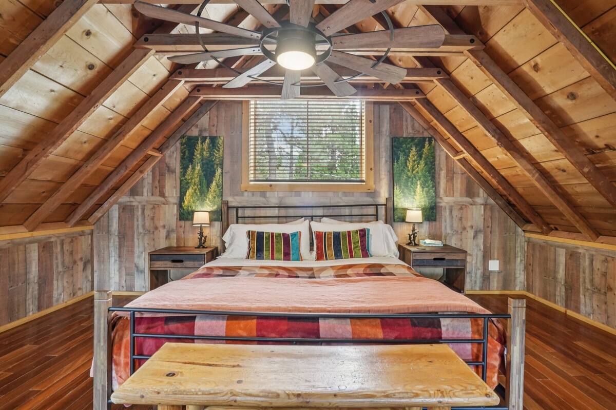 A wooden attic bedroom with a bed, nightstands, and a ceiling fan.