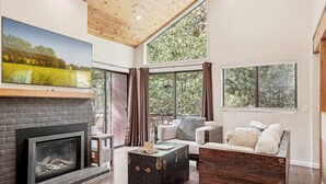 A spacious living room with a fireplace, large windows, and a cozy seating area. - Idyllwild Realty Vacations (Idyllwild)