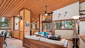 A spacious living area with wooden walls and ceiling, a sofa, a dining table, and a kitchen in the background. - Idyllwild Realty Vacations (Idyllwild)