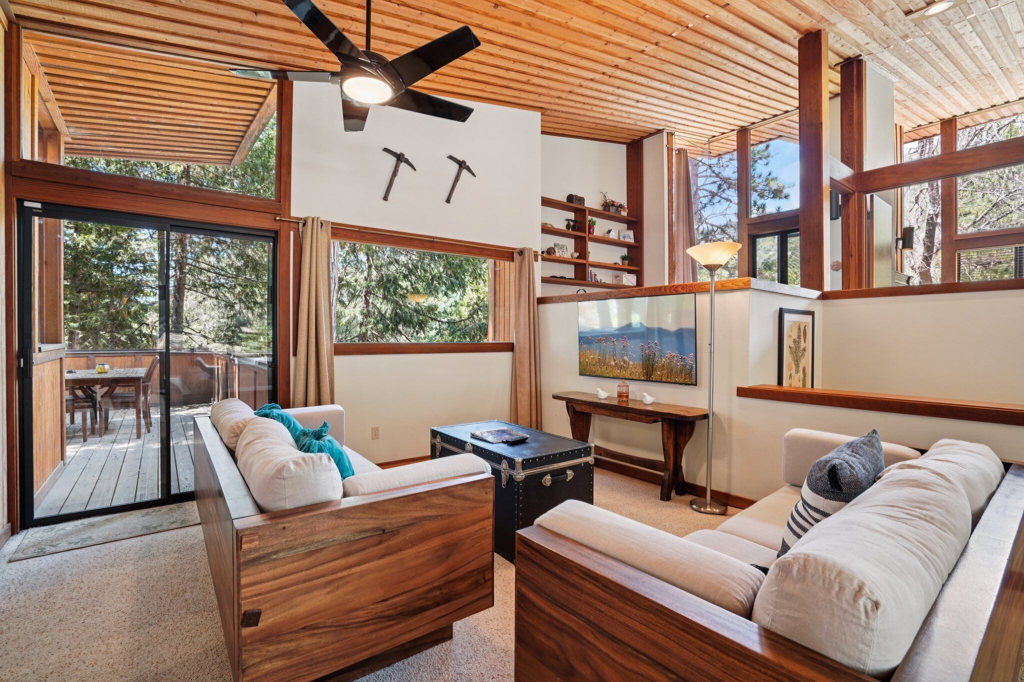 Ein geräumiges Wohnzimmer mit Holzmöbeln, großen Fenstern und einem Deckenventilator.