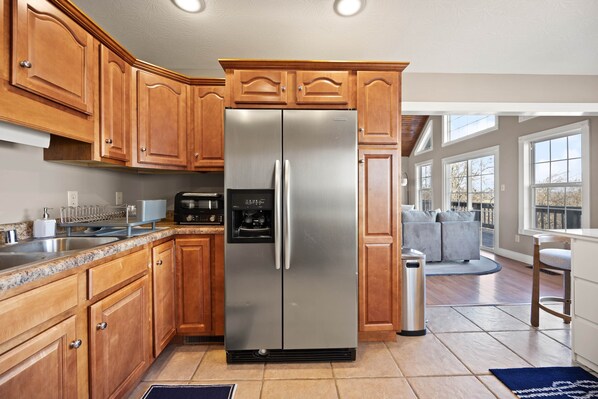 A kitchen with wooden cabinets, a stainless steel refrigerator, a coffee maker, and a trash can. - Frank's Bird House (Pulaski County)