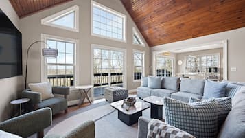 A spacious living room with a high ceiling, large windows, and a cozy seating area.