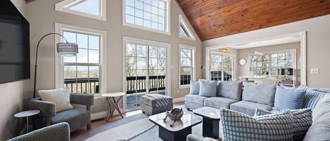 A spacious living room with a high ceiling, large windows, and a cozy seating area.