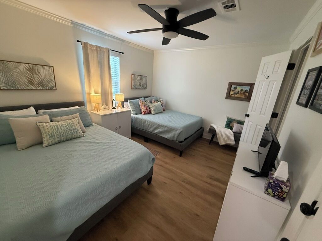 Une chambre avec deux lits, un ventilateur de plafond, un bureau et une armoire.