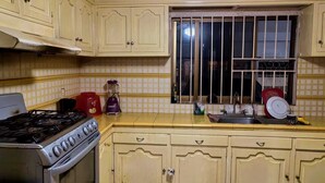 Une cuisine équipée d’une cuisinière à gaz, d’un four, d’un mixeur et d’une fenêtre avec des barreaux.