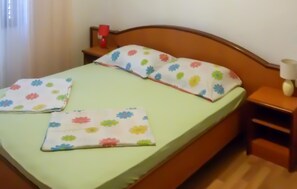 Un lit avec une couvre-lit à motifs floraux et des oreillers, une table de chevet avec une lampe, et une fenêtre avec des rideaux.