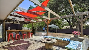 En udendørs træterrasse med en pergola, røde og hvide stribede parasoller og grillområde.