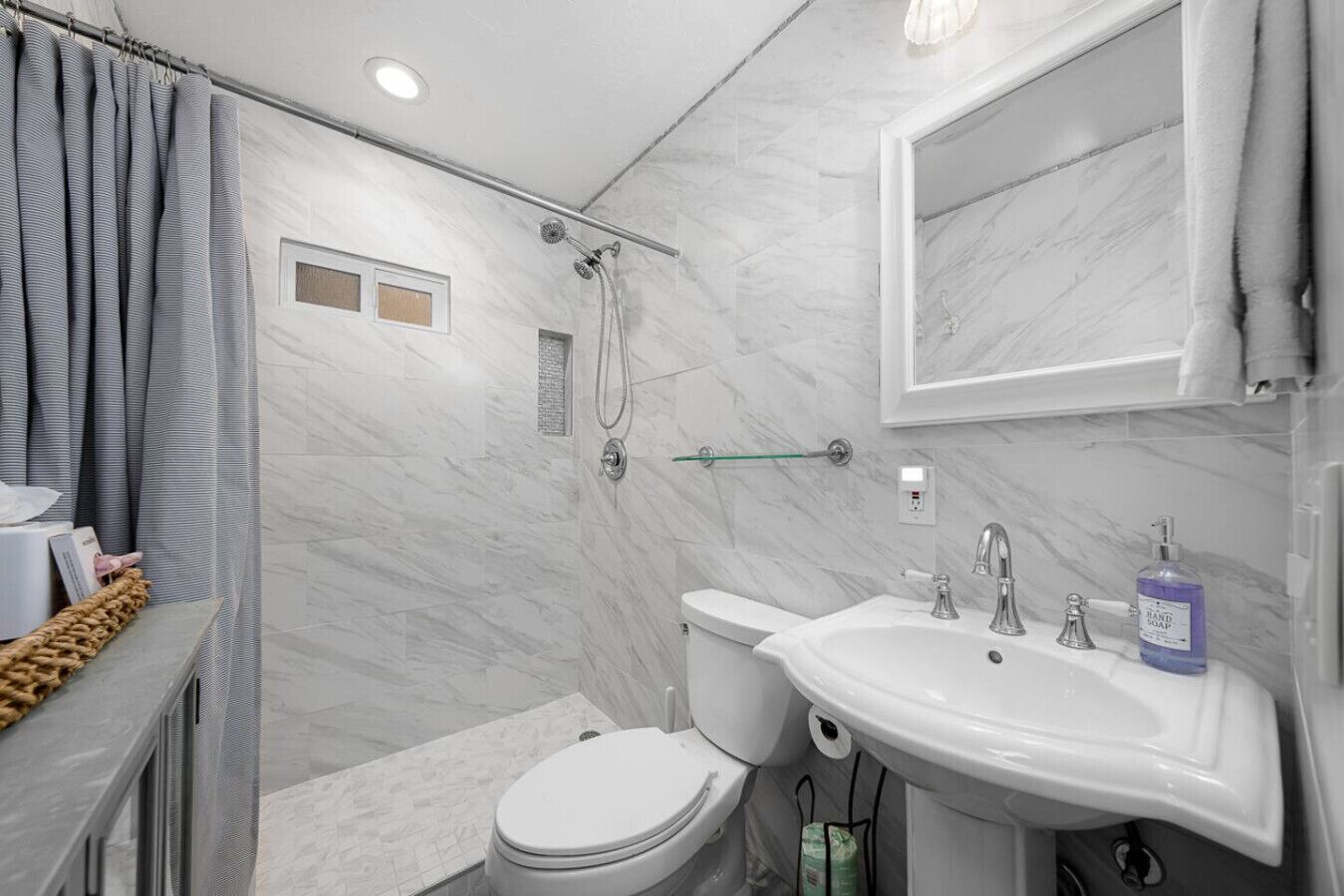 Een badkamer met douche, toilet, wastafel en marmeren wanden.
