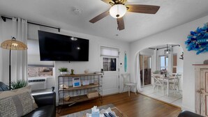 Ein Wohnzimmer mit einer Couch, Fernseher, Deckenventilator und einem Essbereich mit Stühlen und einem Tisch.