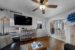 A living room with a sofa, TV, ceiling fan, and a dining area with chairs and a table. - Homey Cottage w/ Ocean View Patio (San Diego)