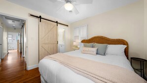 Ein Schlafzimmer mit einem großen Bett, einem Deckenventilator, einer Schiebetür im Scheunenstil und Blick auf einen Flur.
