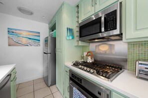 A kitchen with teal cabinets, a stainless steel microwave, a gas stove, and a refrigerator. - Homey Cottage w/ Ocean View Patio (San Diego)