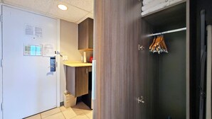 Een hotelkamer met een witte deur, een houten kast, een kleine badkamer en een handdoekrek met houten hangers.