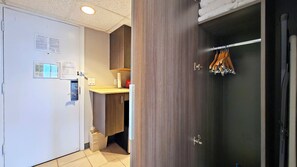 Ein Hotelzimmer mit weißer Tür, einem Holzschrank, einem kleinen Badezimmer und einem Handtuchhalter mit hölzernen Kleiderbügeln.