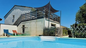 Une piscine avec des chaises longues, un bâtiment doté d’un toit en pente et une clôture.