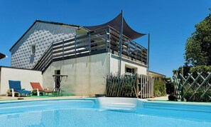 A swimming pool with lounge chairs, a building with a sloped roof, and a fence.