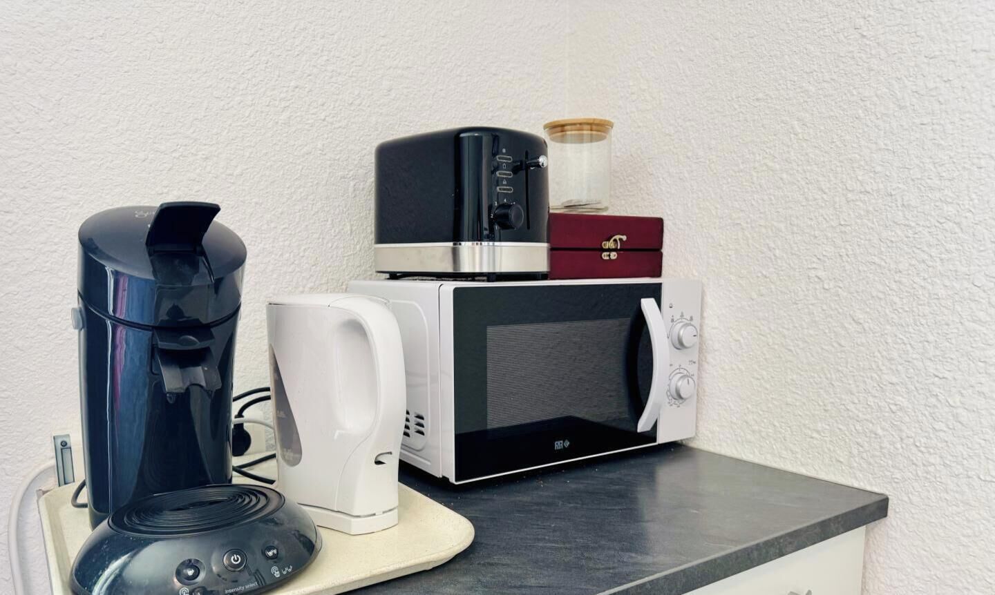 Et køkken med kaffemaskine, mikroovn og brødrister på bordpladen.