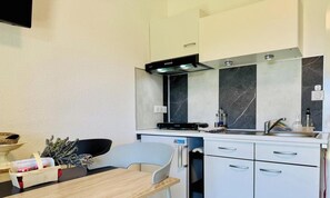 A compact kitchen with a microwave, stove, and sink. There is a small refrigerator, a dining table with chairs, and a basket with items on the table.