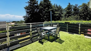 Un espace extérieur aménagé avec une table et des chaises, entouré d’une clôture en bois et de verdure.