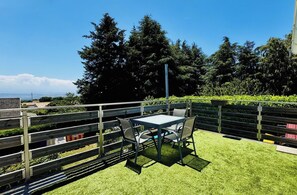 An outdoor seating area with a table and chairs, surrounded by a wooden fence and greenery.