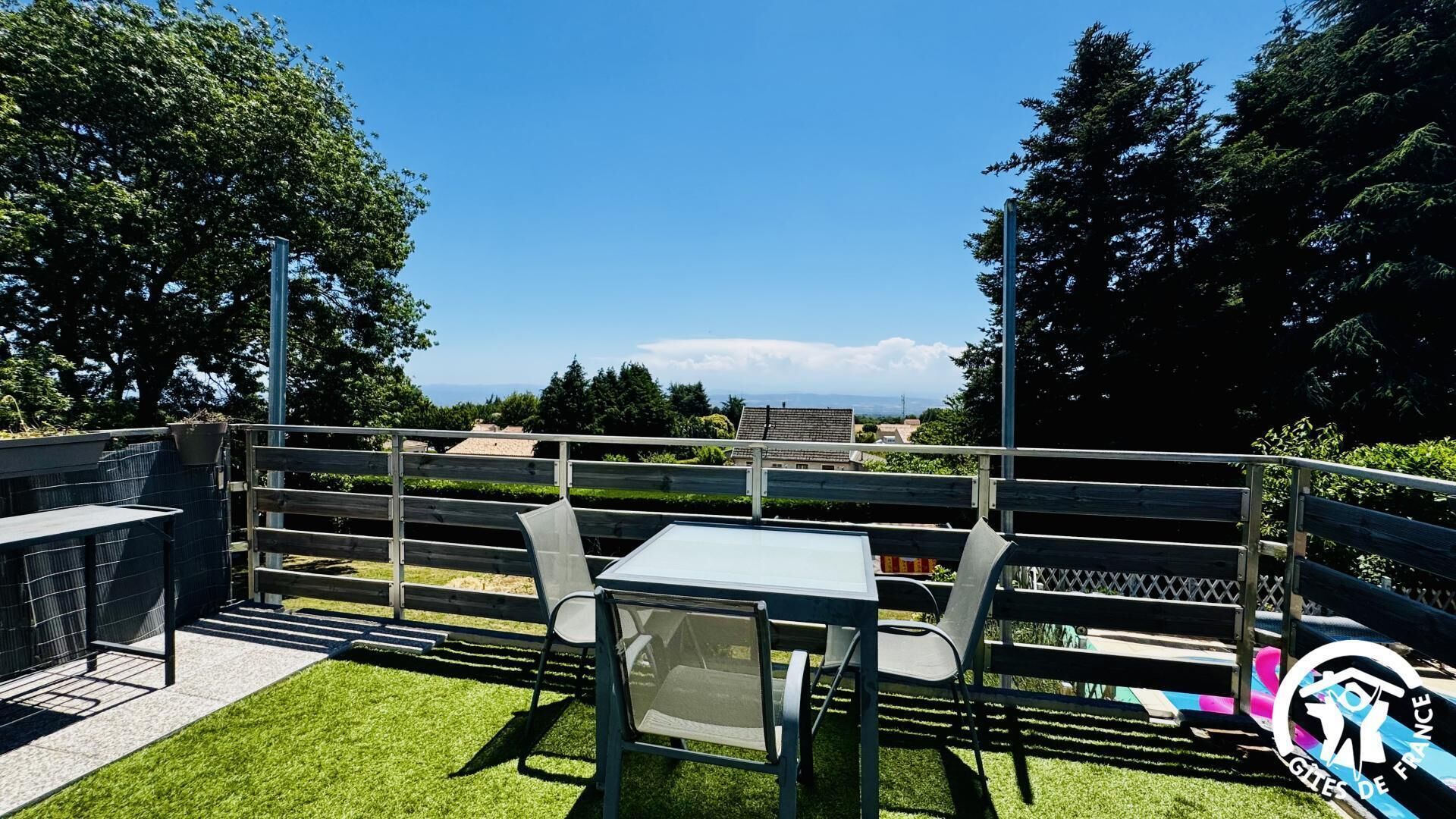 A terrace with a table and chairs, a view of the landscape, and a logo in the corner.