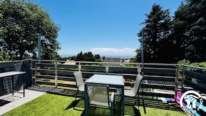 A terrace with a table and chairs, a view of the landscape, and a logo in the corner.