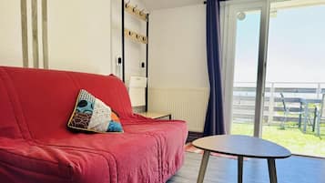 Een rode bank met een gekleurd kussen, een kleine tafel en uitzicht op een balkon met een hekwerk.