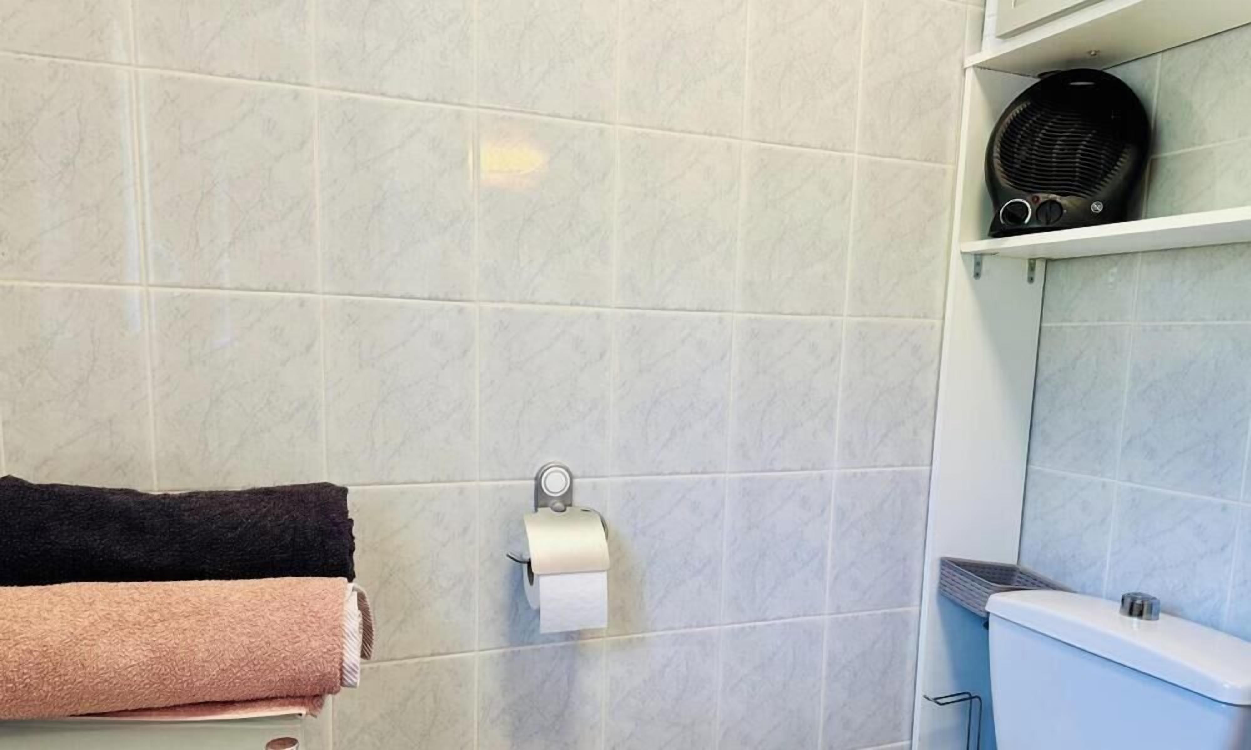Un baño con inodoro, un perchero con toallas y un dispensador de toallas de papel.