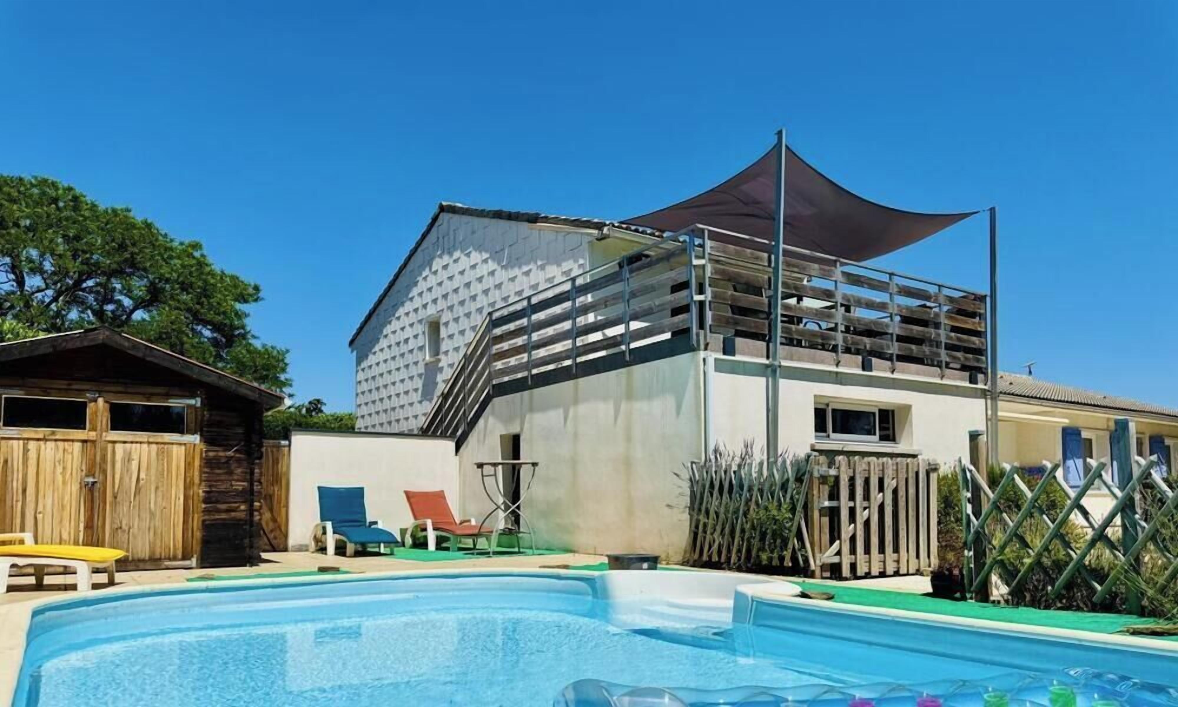 Un espace piscine avec une maison, une clôture en bois et un coin ombragé.
