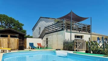 Un espace piscine avec une maison, une clôture en bois et un coin ombragé.
