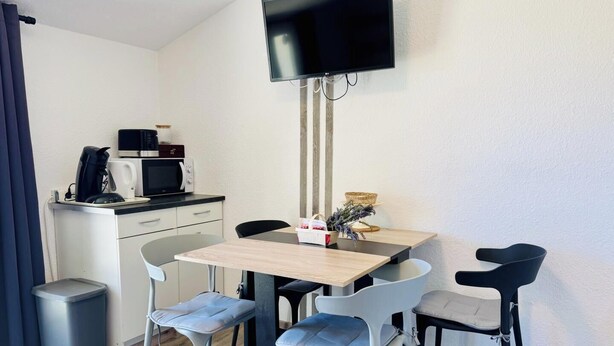 Une petite cuisine équipée d ’un four à micro-ondes, d’une machine à café et d’un grille-pain. On y trouve une table avec quatre chaises et un téléviseur fixé au mur.