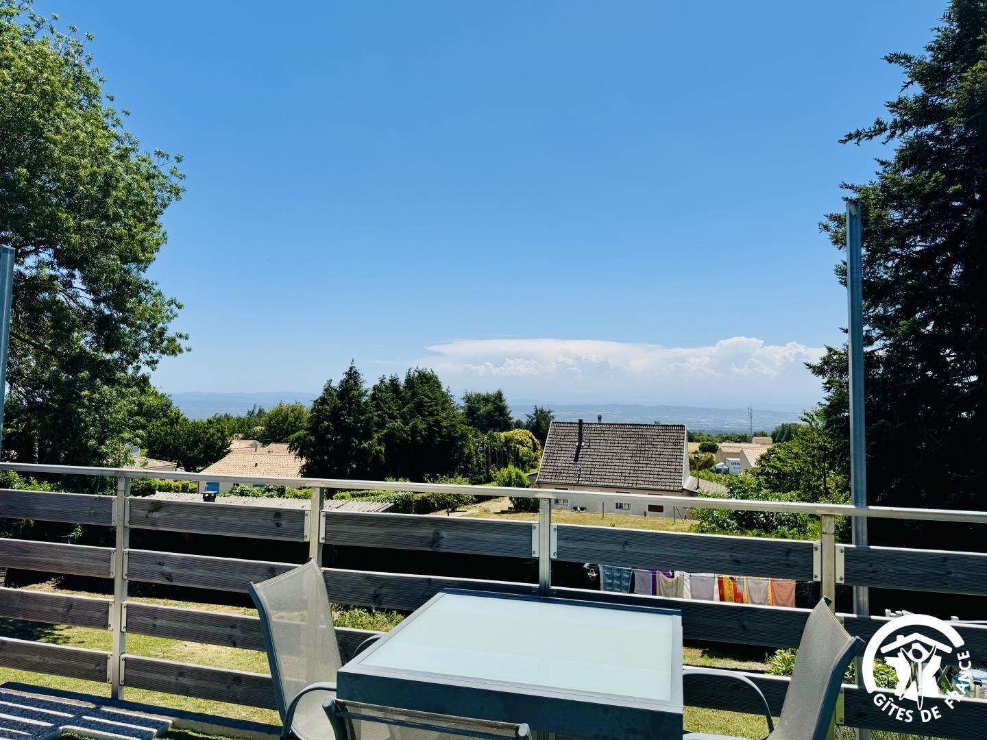 Une terrasse avec une table et des chaises, donnant sur un paysage composé d’arbres et de bâtiments.