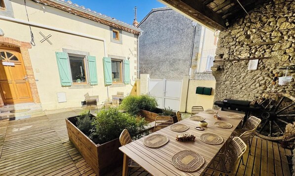 Eine Terrass mit Holztable, gedeckt für ein Essen, umgeben von Korbstühlen und einer Steinsäule im Hintergrund.