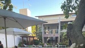 Ein Poolbereich mit Liegestühlen und Sonnenschirmen, umgeben von Grünflächen und einem Gebäude im Hintergrund.
