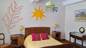 Un dormitorio con cama, dos mesitas de noche, una silla, un escritorio, una lámpara colgante y un adorno en la pared.