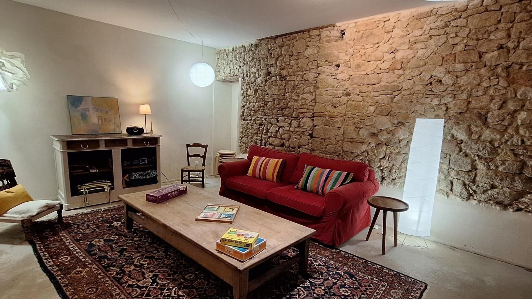 A living room with a red sofa, a coffee table with books, a stone wall, and a lamp.
