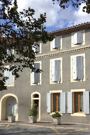 Un edificio con varias ventanas, algunas con contraventanas, y una entrada central con un arco.