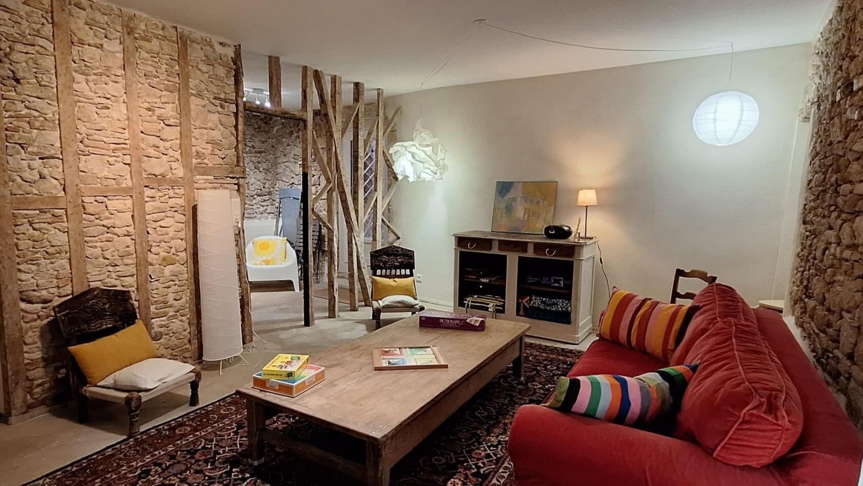 A living room with a wooden coffee table, a red sofa, a stone wall, and a hanging chair.