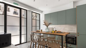Een moderne keuken met een eethoek, met een houten tafel en stoelen, een vaas met gedroogde bloemen en uitzicht door grote glazen deuren.