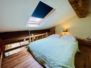 Une chambre avec un puits de lumière, un lit avec des oreillers, une lampe de chevet et un plancher en bois.