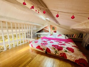 Ein Schlafzimmer mit Holzboden, einem Bett mit floralem Bettzeug, einem weißen Geländer und einer Decke mit roten Pendelleuchten.